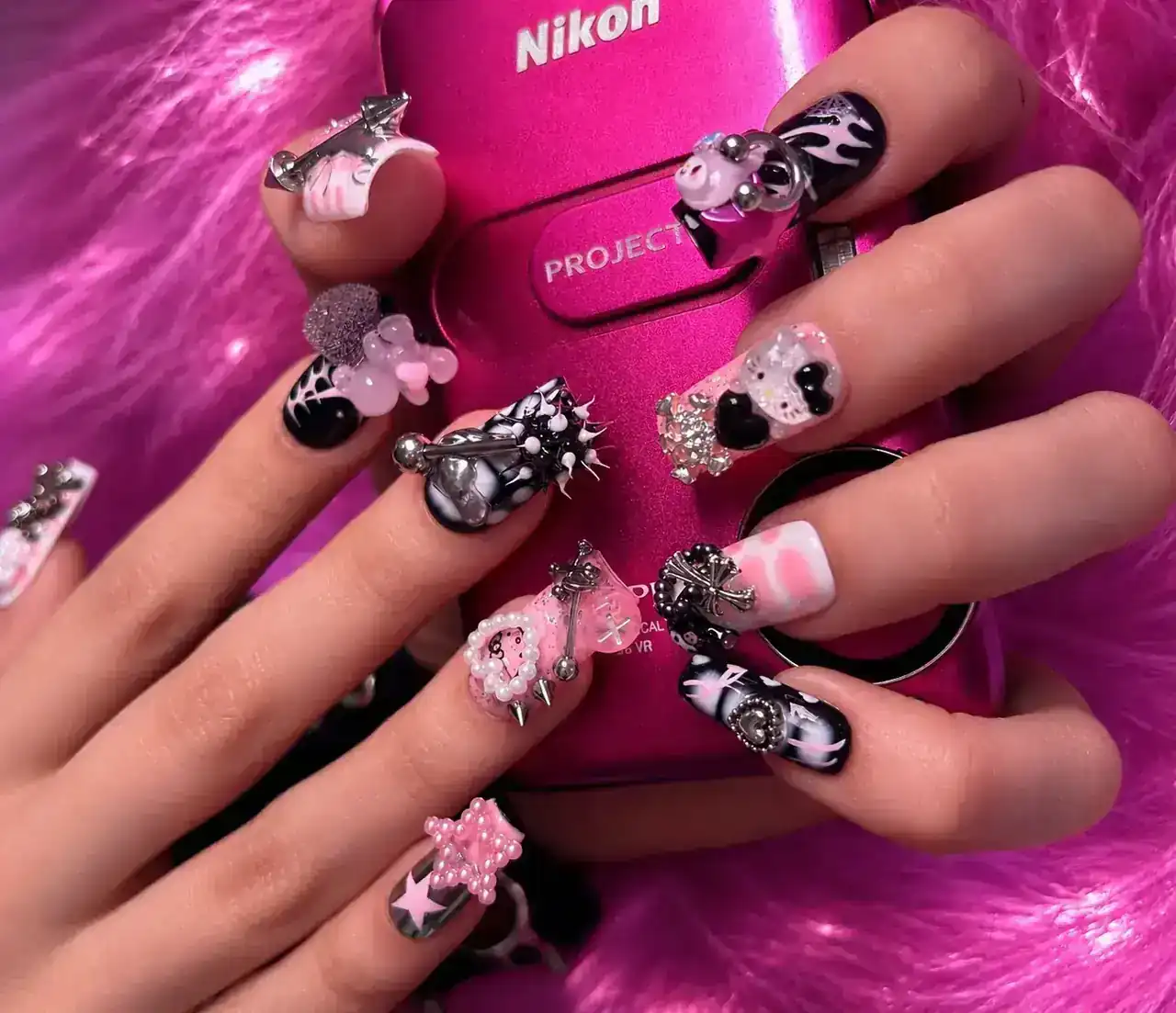 Pink and black nail styling holding a pink camera.