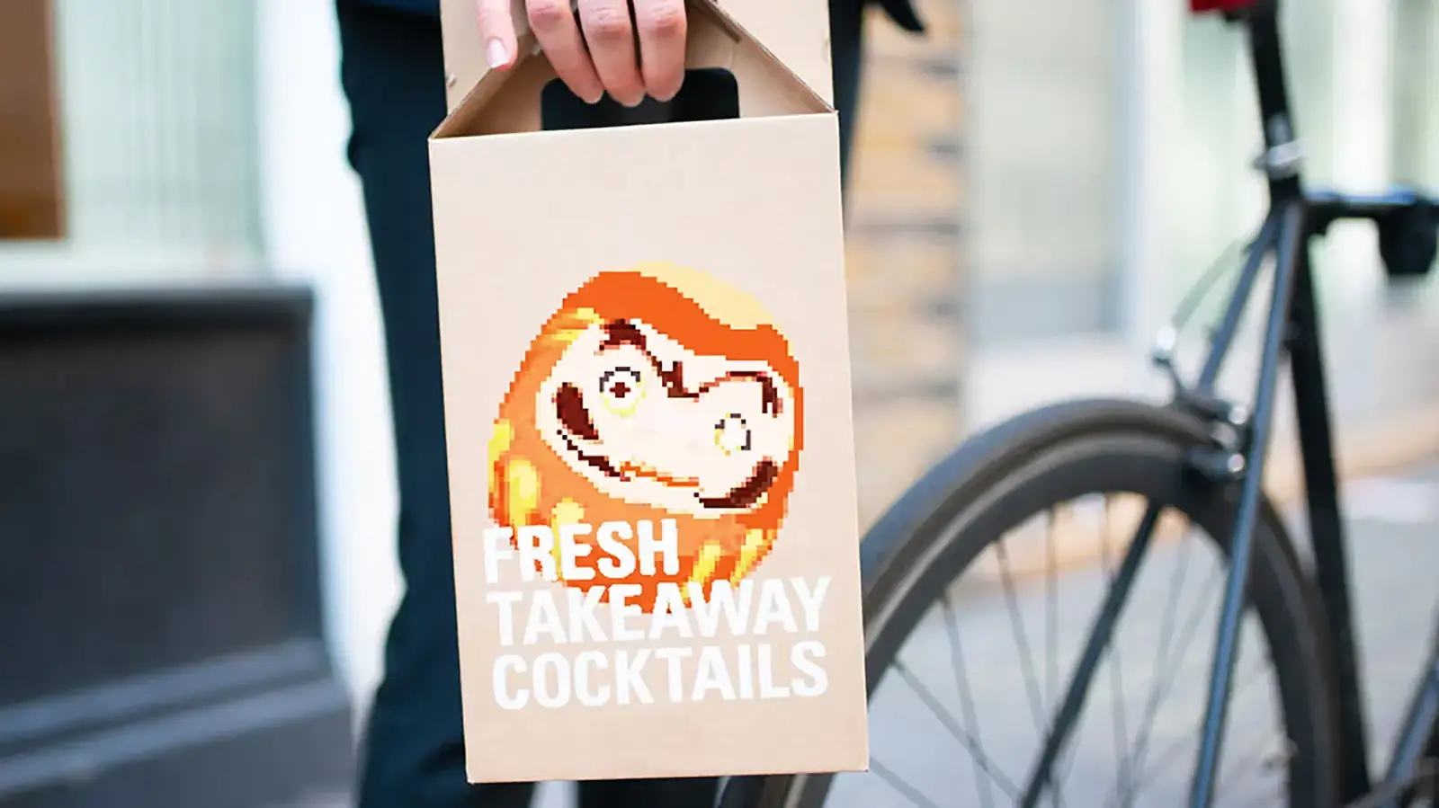 A hand holding the cocktail delivery box by its handle beside a bicycle